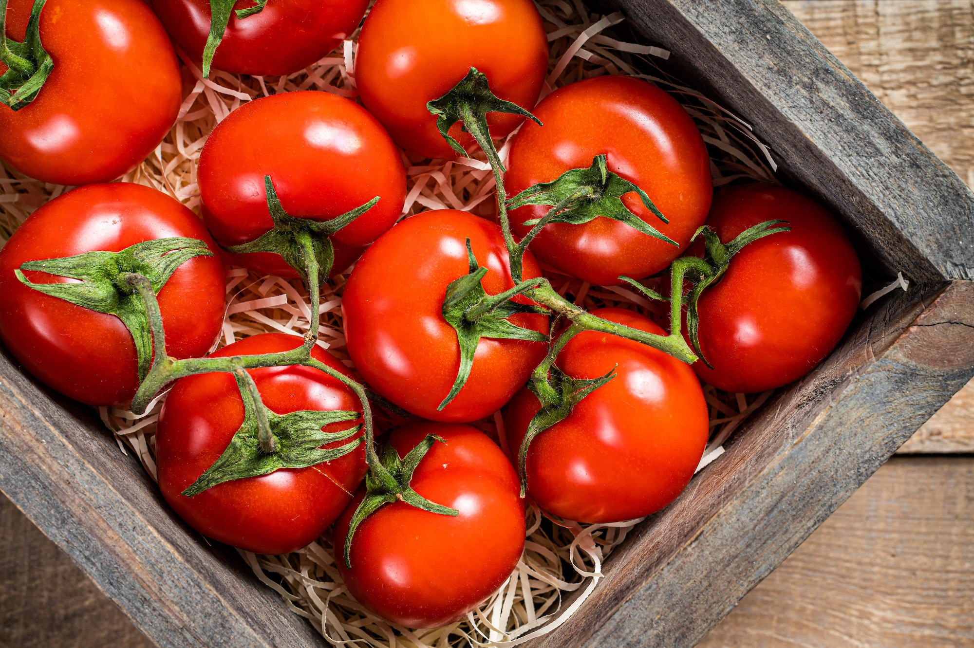 Ripe Red tomatoes in wooden market box. Wooden background. Top view